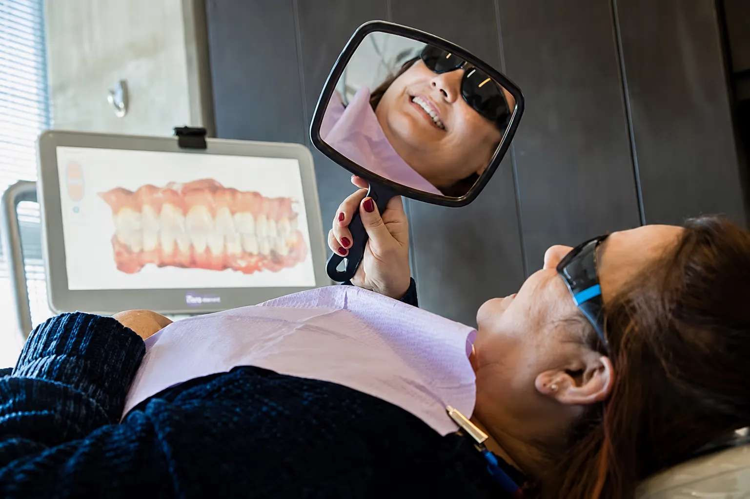 A relaxed patient checking her smile in a hand mirror at Avanti Dentistry